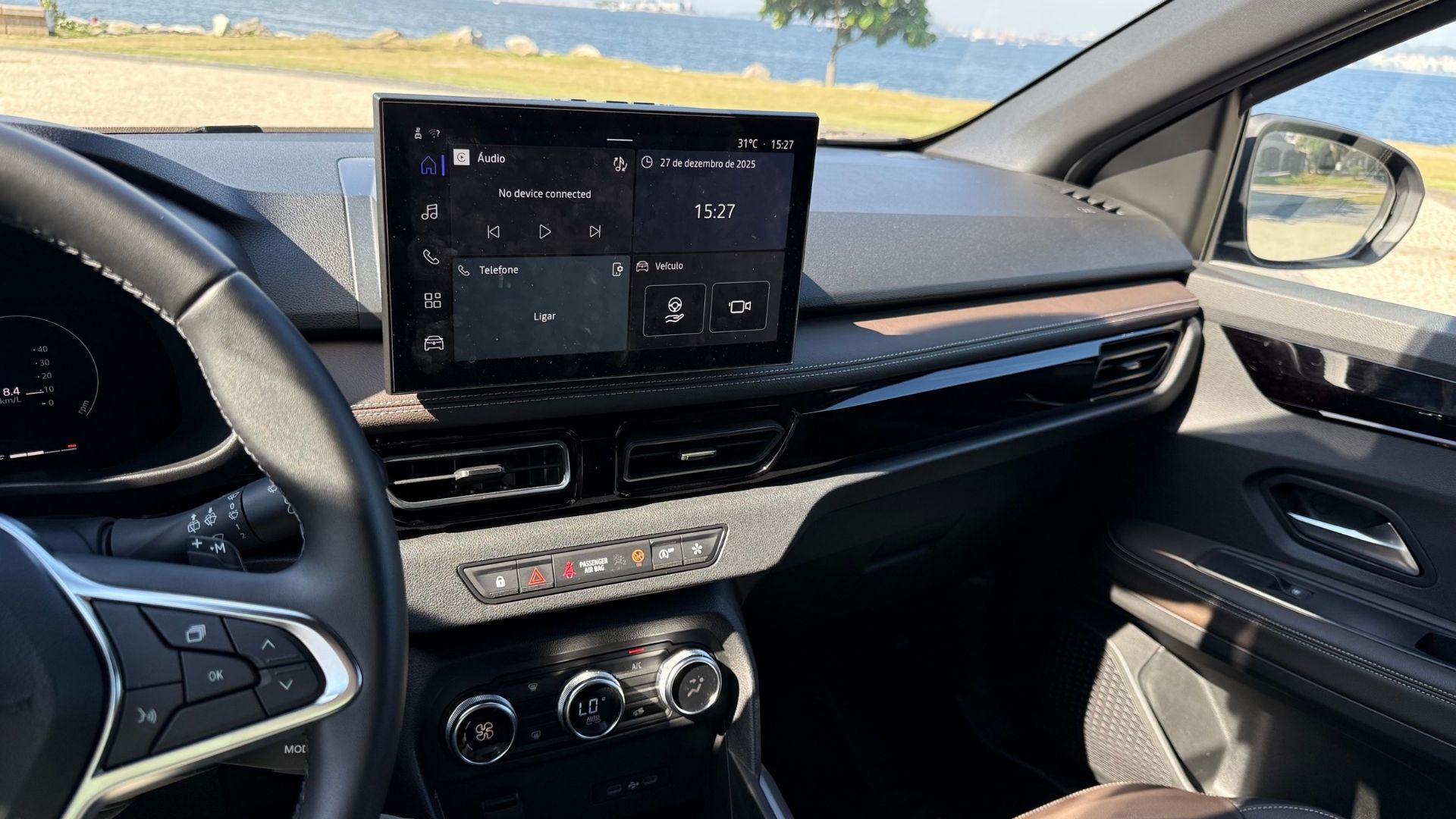 Interior view of a modern car showcasing a digital display with audio and connectivity options, leather accents, and a scenic view of water in the background.
