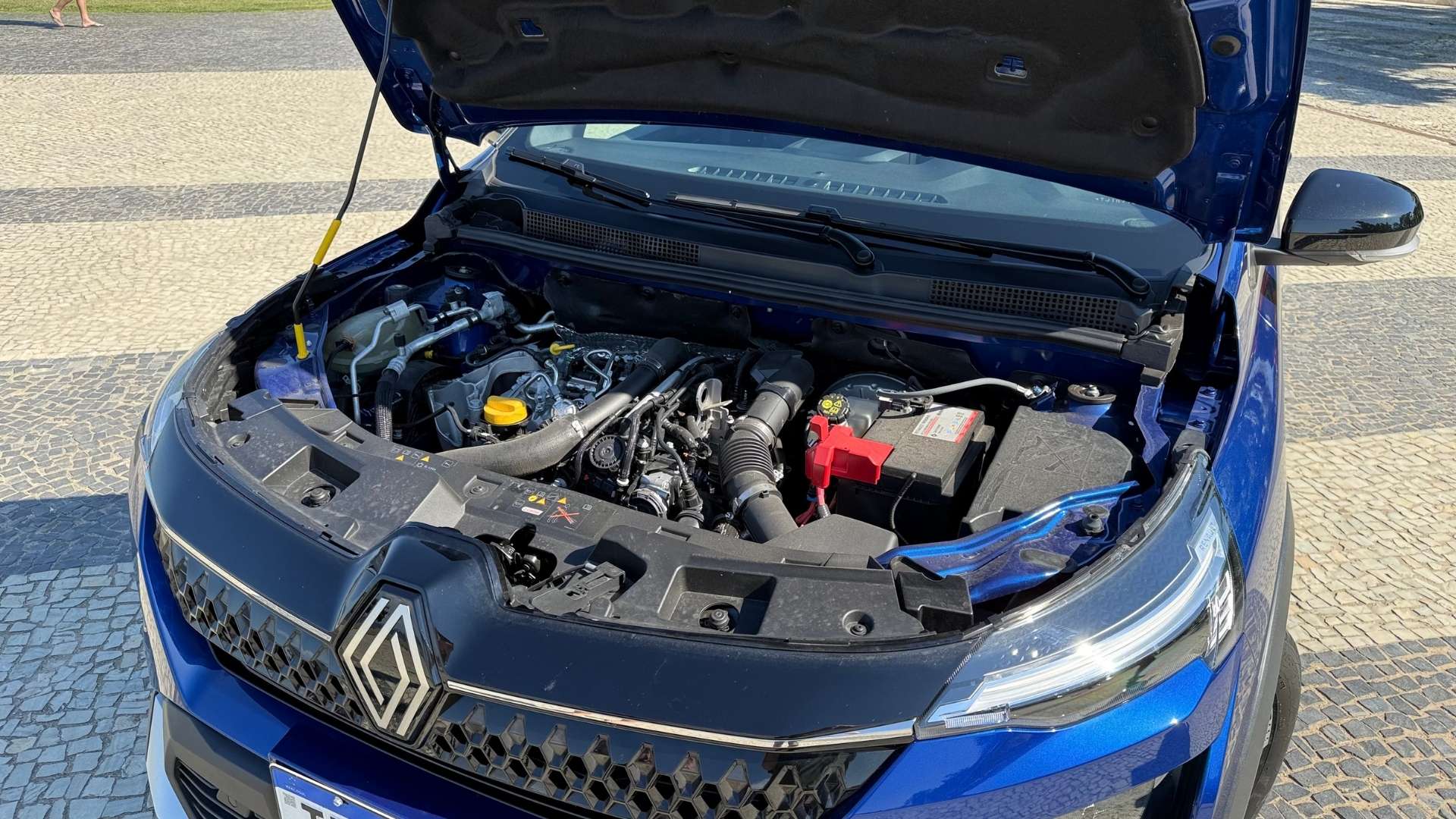 Close-up of a car engine compartment with the hood lifted, showcasing various engine components and a battery.