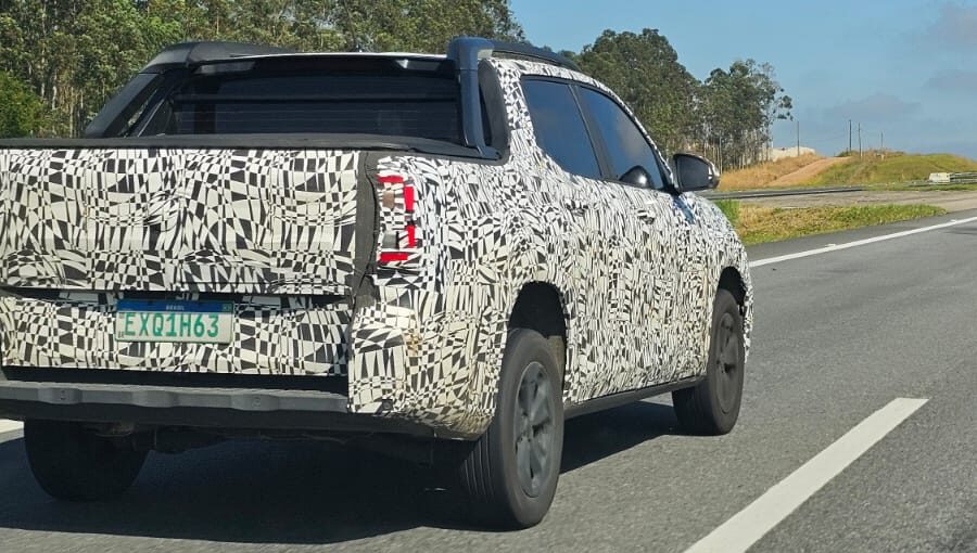 A camouflaged pickup truck on a highway, showcasing a unique abstract pattern on its body while driving past green trees and blue sky.