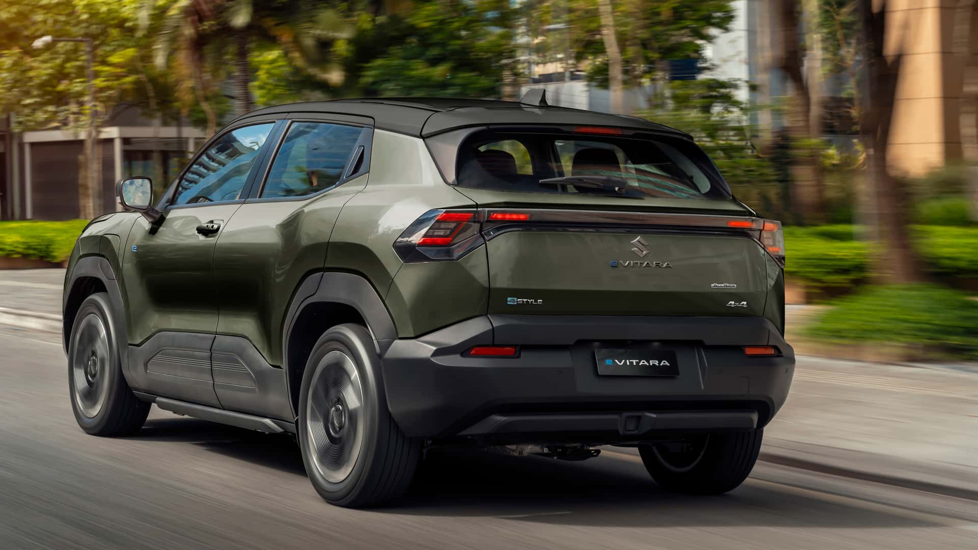 A green Suzuki Vitara SUV driving along a city street, showcasing its modern design and sleek profile.