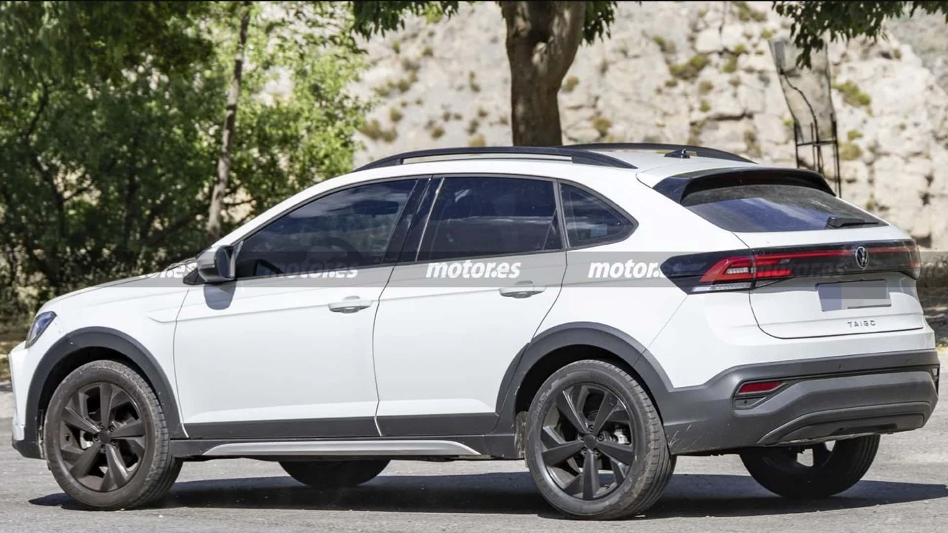 A white SUV with a sleek design, featuring black accents and large alloy wheels, parked on a gravel surface surrounded by greenery.
