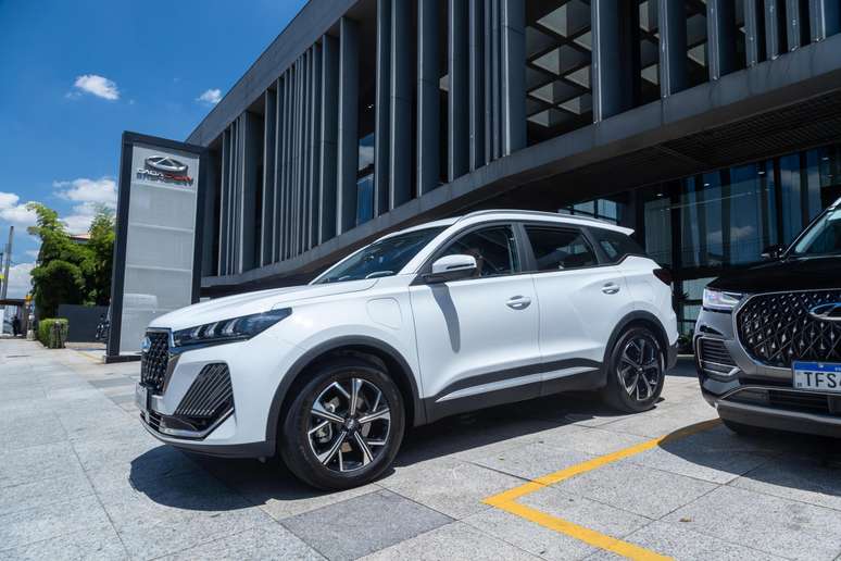 SUV branco estacionado em frente a um edifício moderno com grande fachada de vidro.