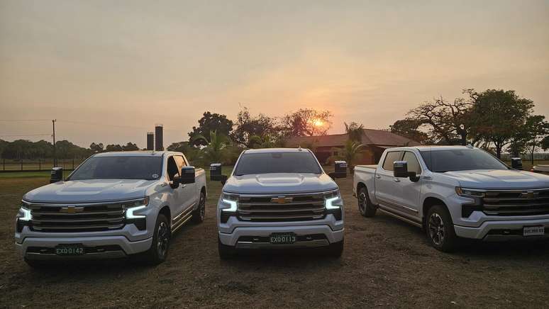 Três caminhonetes Chevrolet brancas em um campo ao pôr do sol.