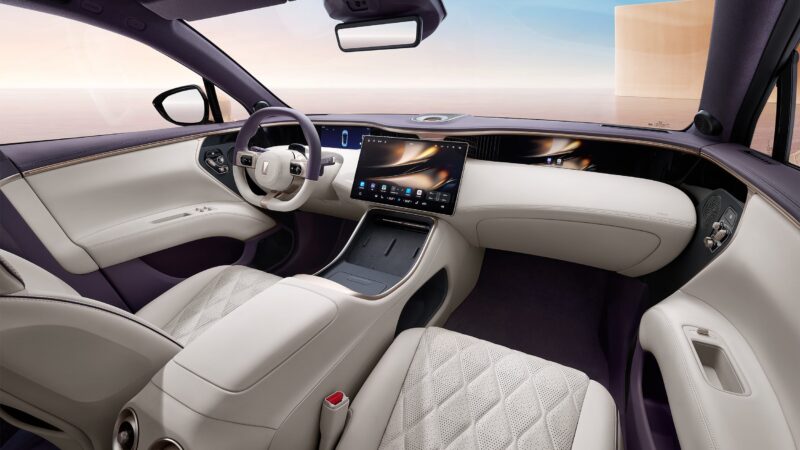 Interior moderno e luxuoso de um carro, apresentando um volante, painel digital e estofamento em couro claro com detalhes roxos.