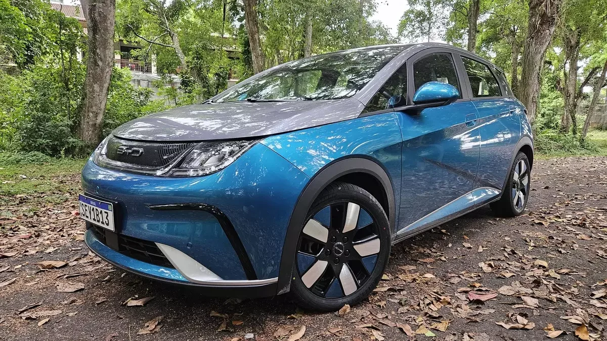 Um carro elétrico azul estacionado em uma estrada cercada por árvores e folhas secas no chão.