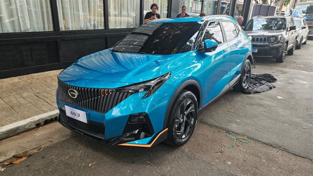 SUV azul estacionado na calçada, com detalhes pretos e laranja, entre outras pessoas e carros ao fundo.