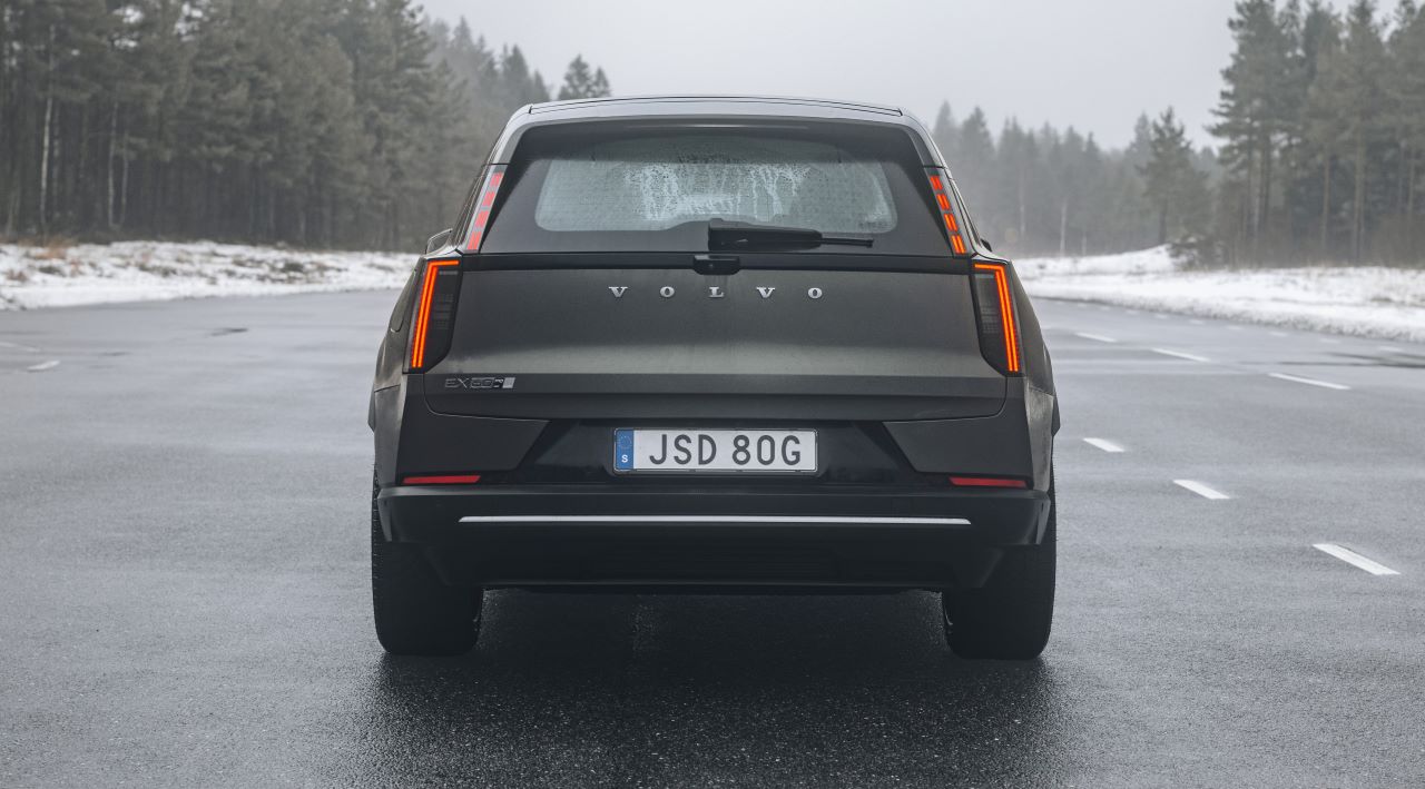 A traseira de um carro da Volvo modelo EX60 em uma estrada molhada, cercado por uma paisagem de árvores e com neve ao redor.