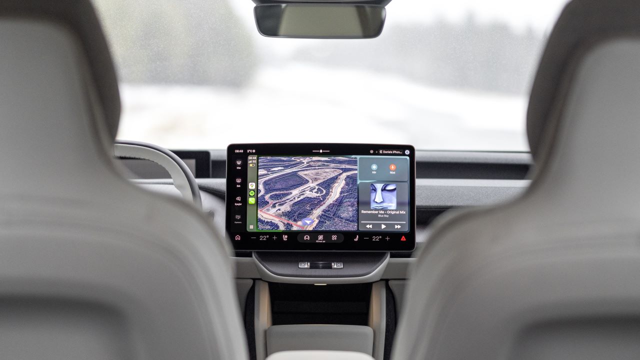 Interior de um carro mostrando o painel com uma tela digital que exibe um mapa e informações de media, visto de trás dos bancos dianteiros.