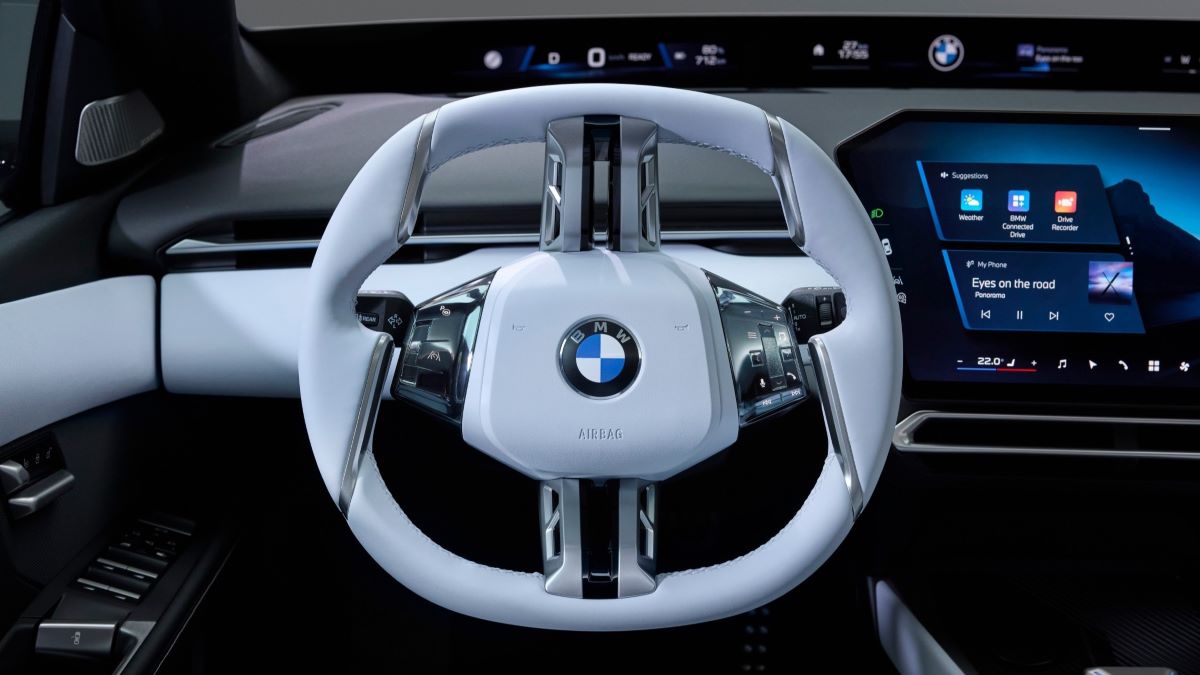 Volante de carro BMW moderno com acabamento em couro branco e tela digital ao fundo.