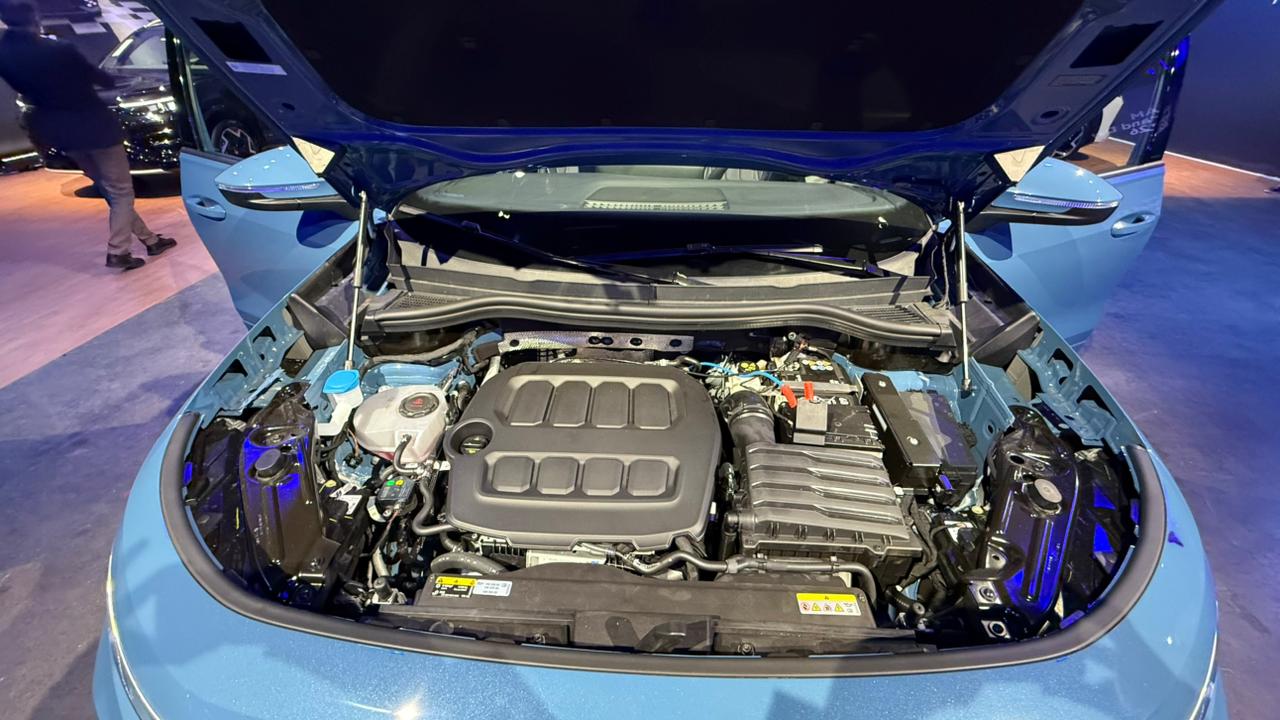 Visão do motor de um carro com capô aberto, mostrando componentes como o bloco do motor, bateria e sistema de refrigeração.