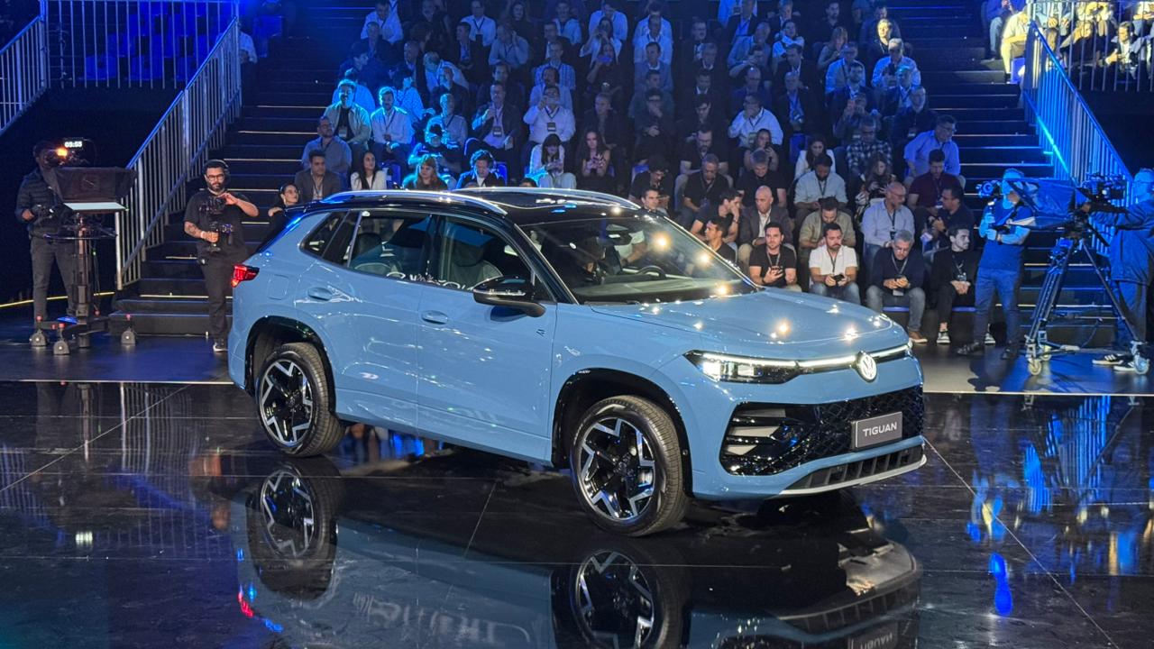Carro azul modelo Tiguan em destaque em um evento, com um público ao fundo e iluminação azul.
