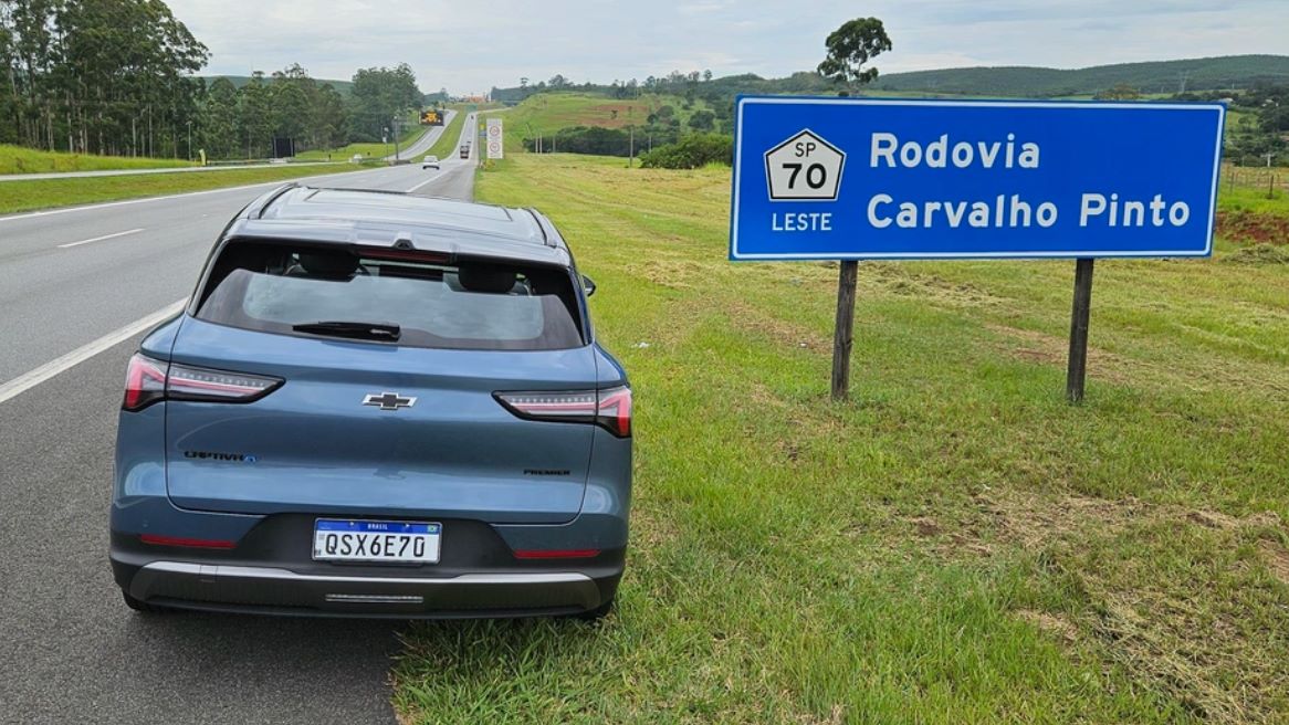 Um carro azul estacionado próximo a um sinal de estrada com a indicação 'Rodovia Carvalho Pinto' e a distância 'SP 70 Leste'.