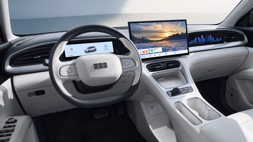 Interior de um carro moderno com volante e painel digital grande, exibindo informações sobre o veículo e uma bela paisagem na tela.