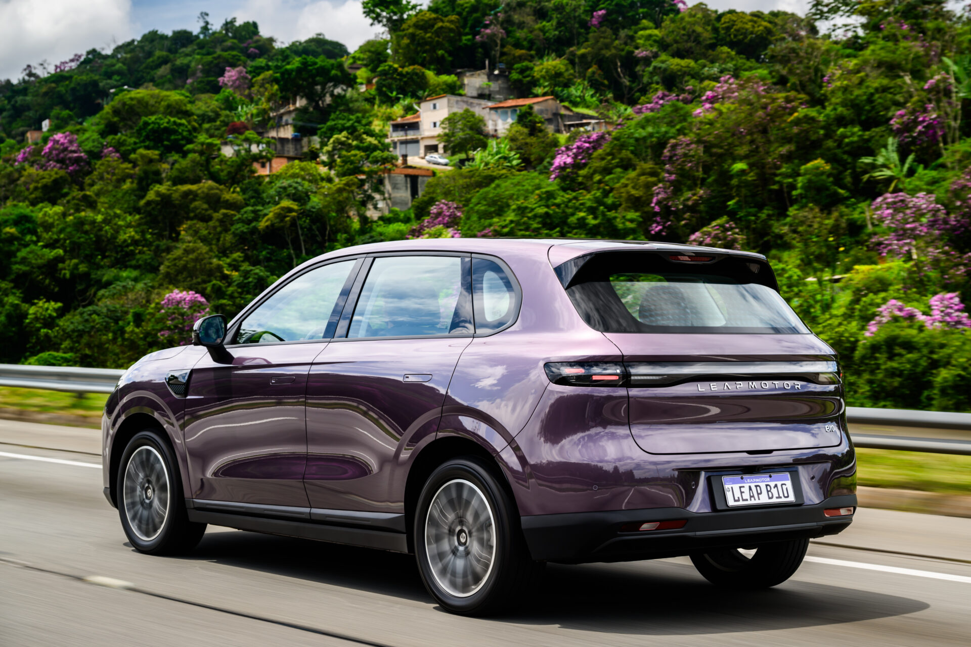 Um carro SUV roxo da Leapmotor em movimento na estrada, com vegetação tropical e flores ao fundo.
