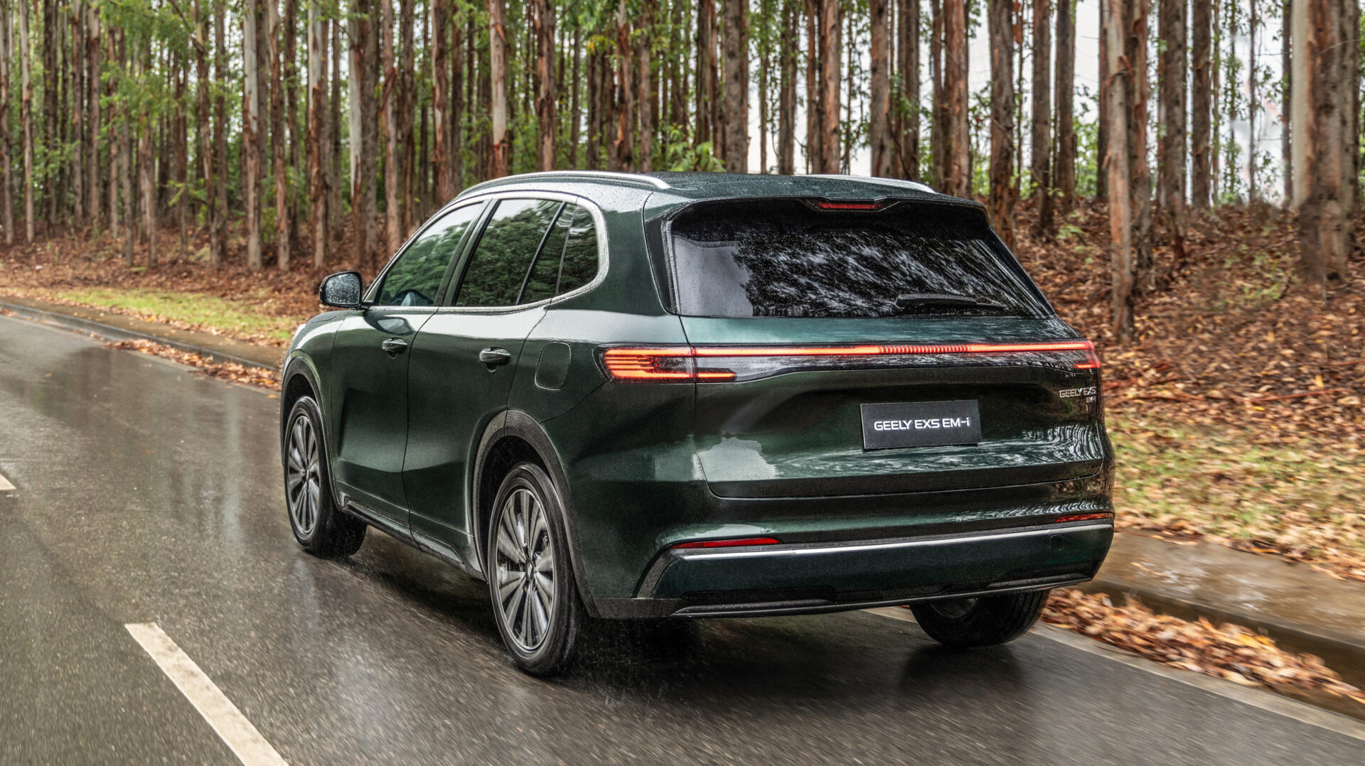 Um SUV verde escuro da Geely, visto de trás, dirigindo em uma estrada molhada com árvores ao fundo.