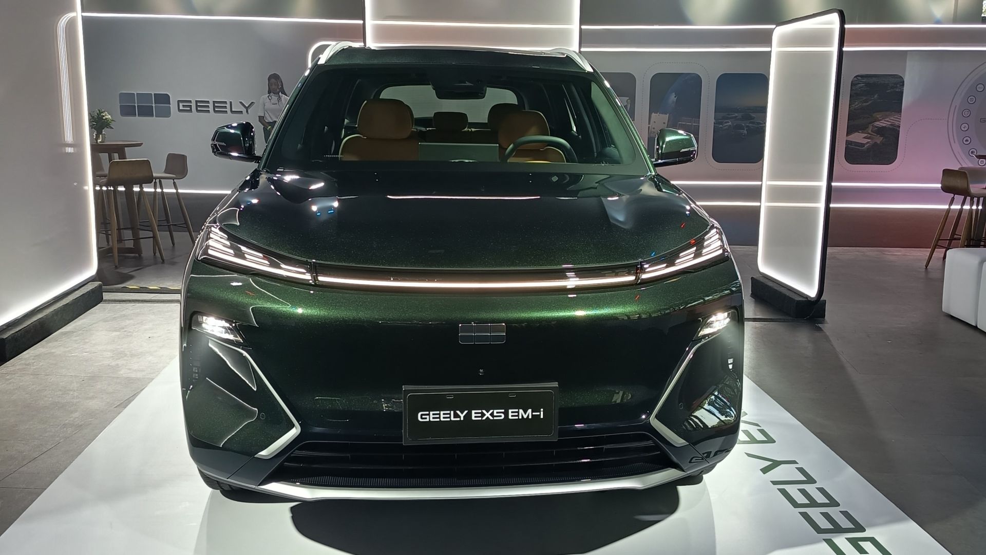 Frente de um carro Geely EX5 EM-i em exibição, com acabamento verde metálico e interior em tom claro.