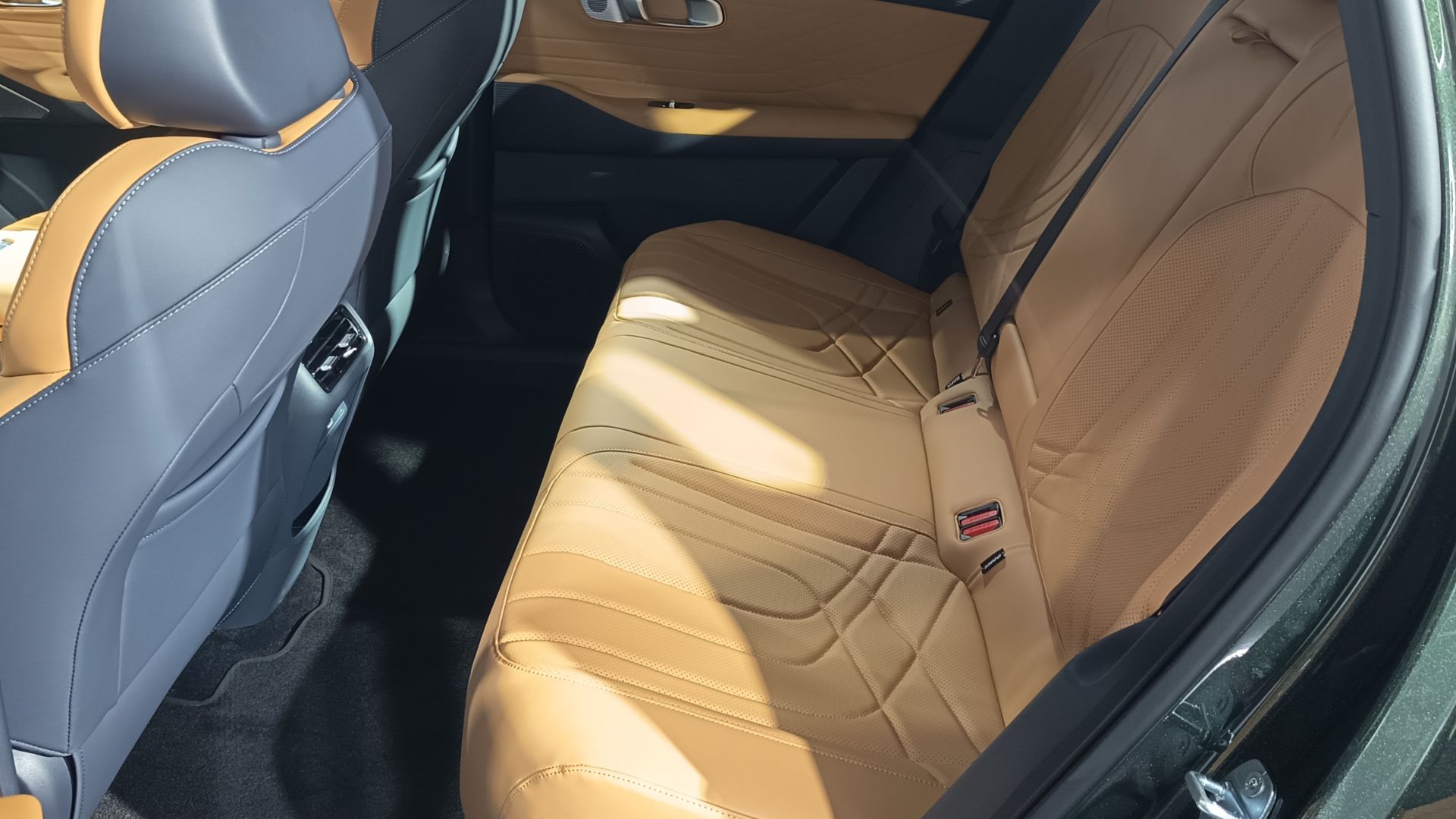 Interior do banco traseiro de um carro, com estofamento em couro bege e detalhes em azul. A luz do sol ilumina os assentos, destacando a textura e o design.