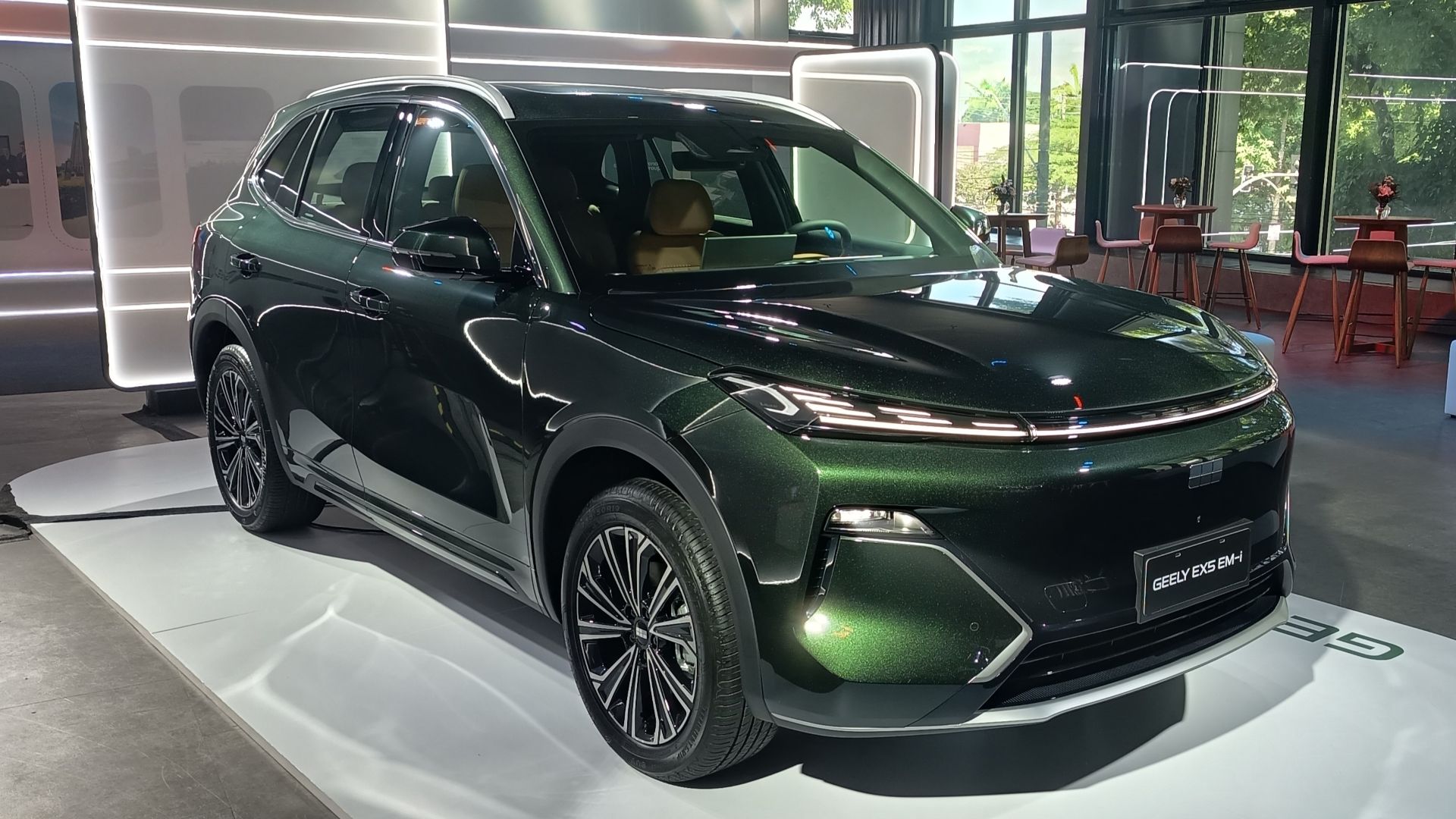 SUV verde escuro da Geely em exposição, com interior claro visível e iluminação moderna ao fundo.