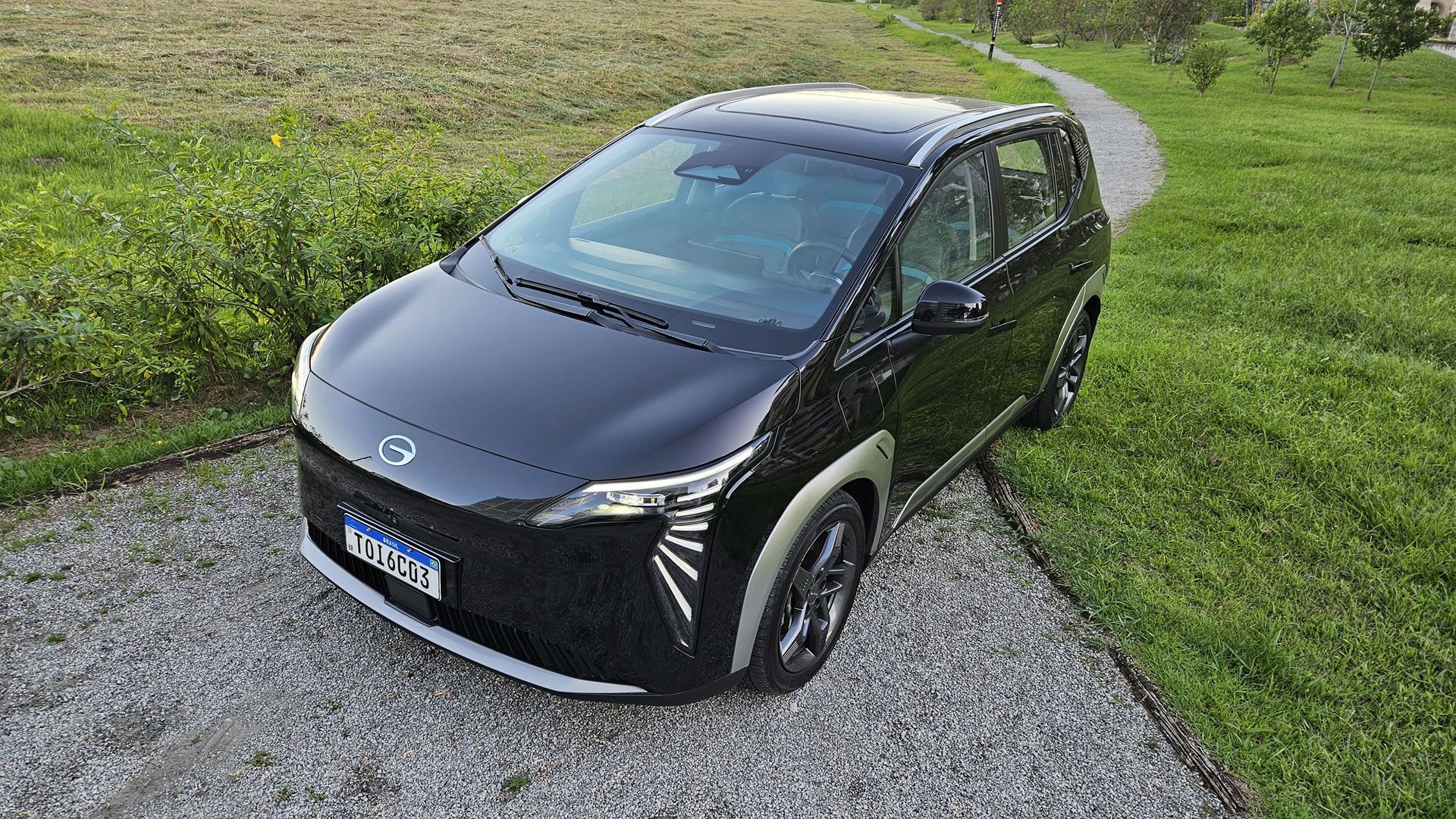 Carro elétrico preto estacionado em um caminho de pedras, cercado por grama e árvores.