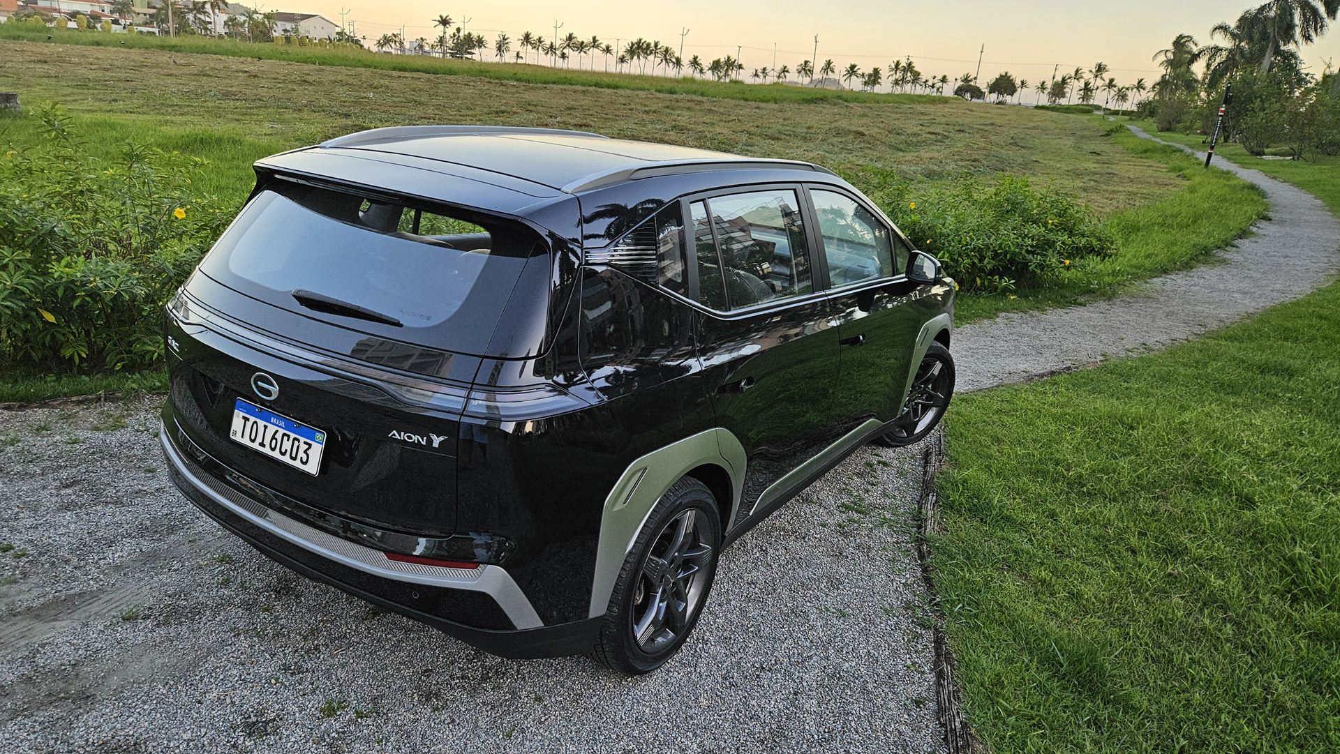 Um carro SUV preto estacionado em um caminho de pedrinhas, com vegetação ao fundo e uma área gramada ao redor.