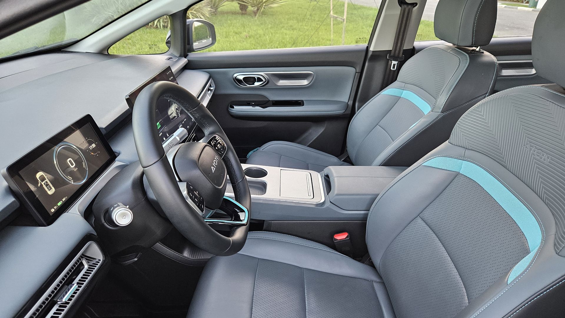 Interior de um carro com volante, painel digital e assentos em tons de cinza e azul.