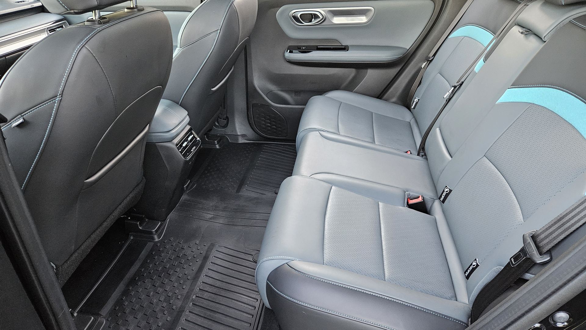 Interior traseiro de um carro, com bancos em couro cinza e azul, mostrando uma visão da parte de trás e do console central.