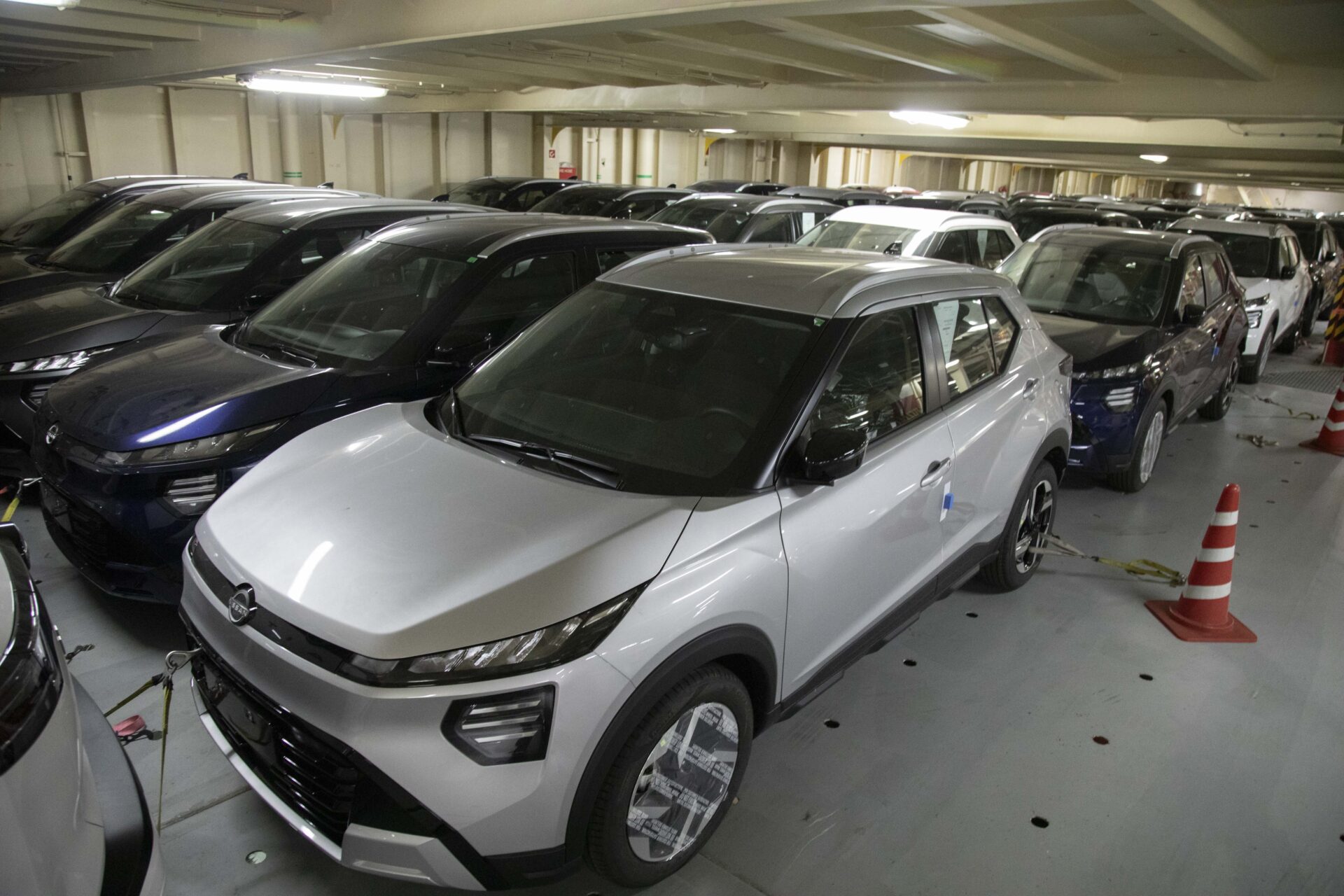 Estacionamento com vários carros, incluindo um veículo prateado em primeiro plano, rodeado por outros automóveis em um ambiente fechado.