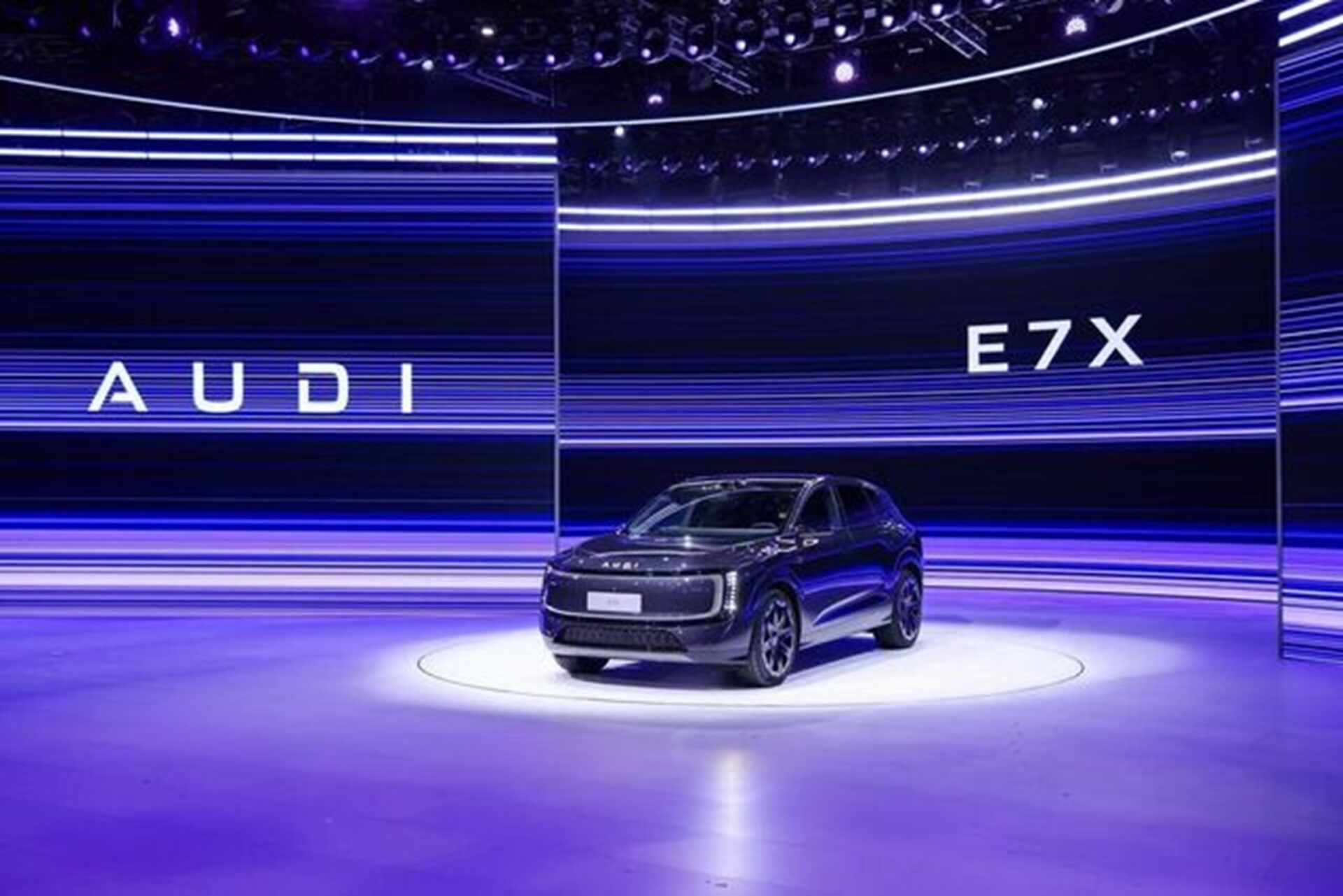 A sleek black Audi E7X showcased on a well-lit stage with vibrant blue and purple lighting and the Audi logo in the background.