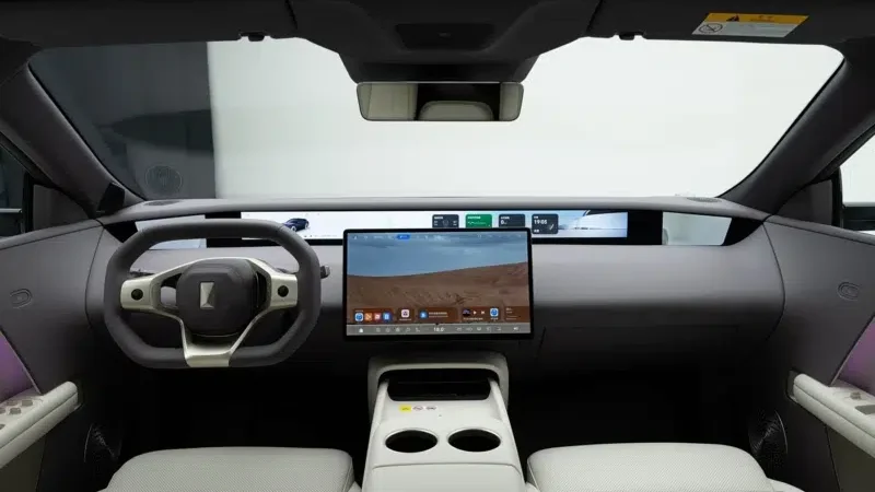 Interior moderno de um carro elétrico, destacando o volante estilizado, um grande painel touchscreen central e bancos claros.