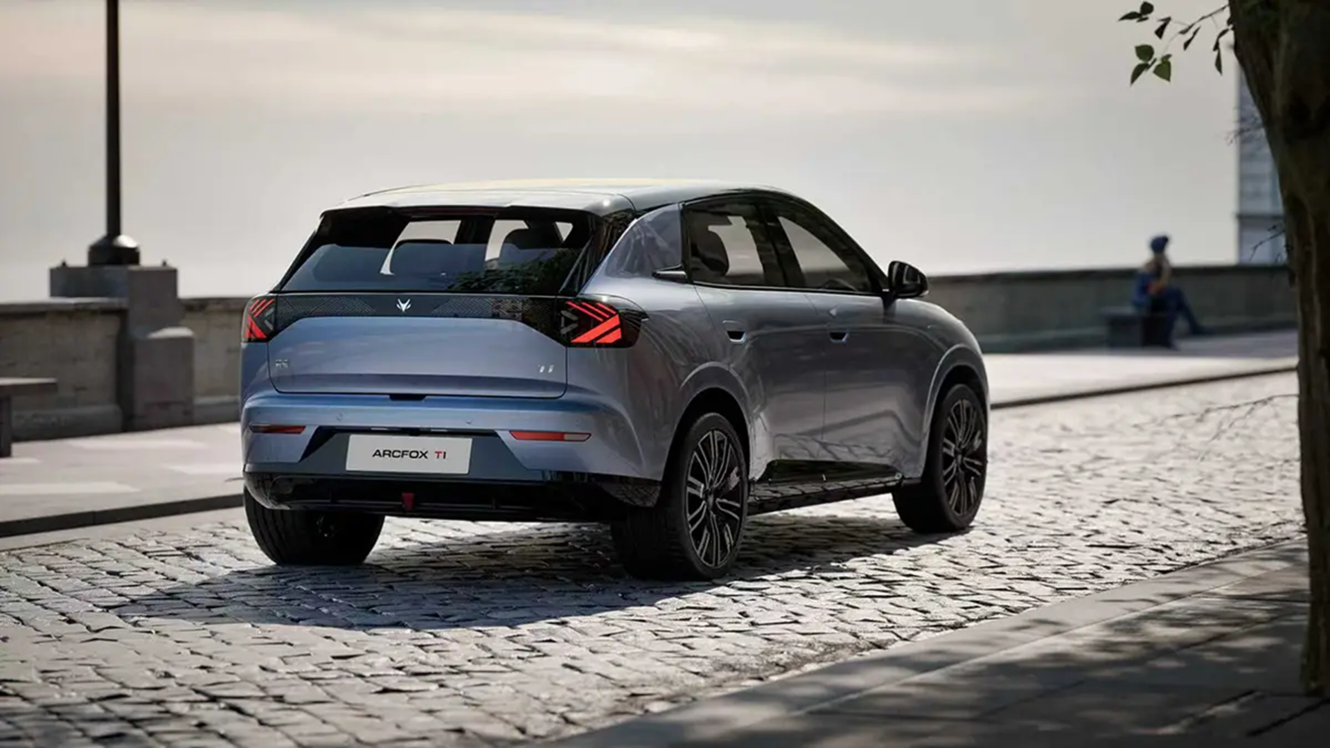 A silver Arcfox T1 electric SUV parked on a cobblestone street, showcasing its sleek rear design and distinctive taillights.