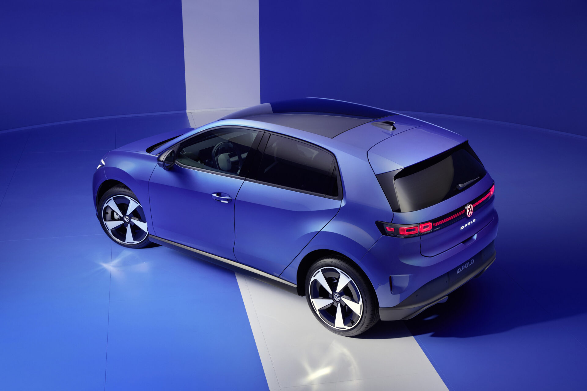 Um carro compacto de cor azul em um fundo azul, exibindo sua parte traseira e lateral.