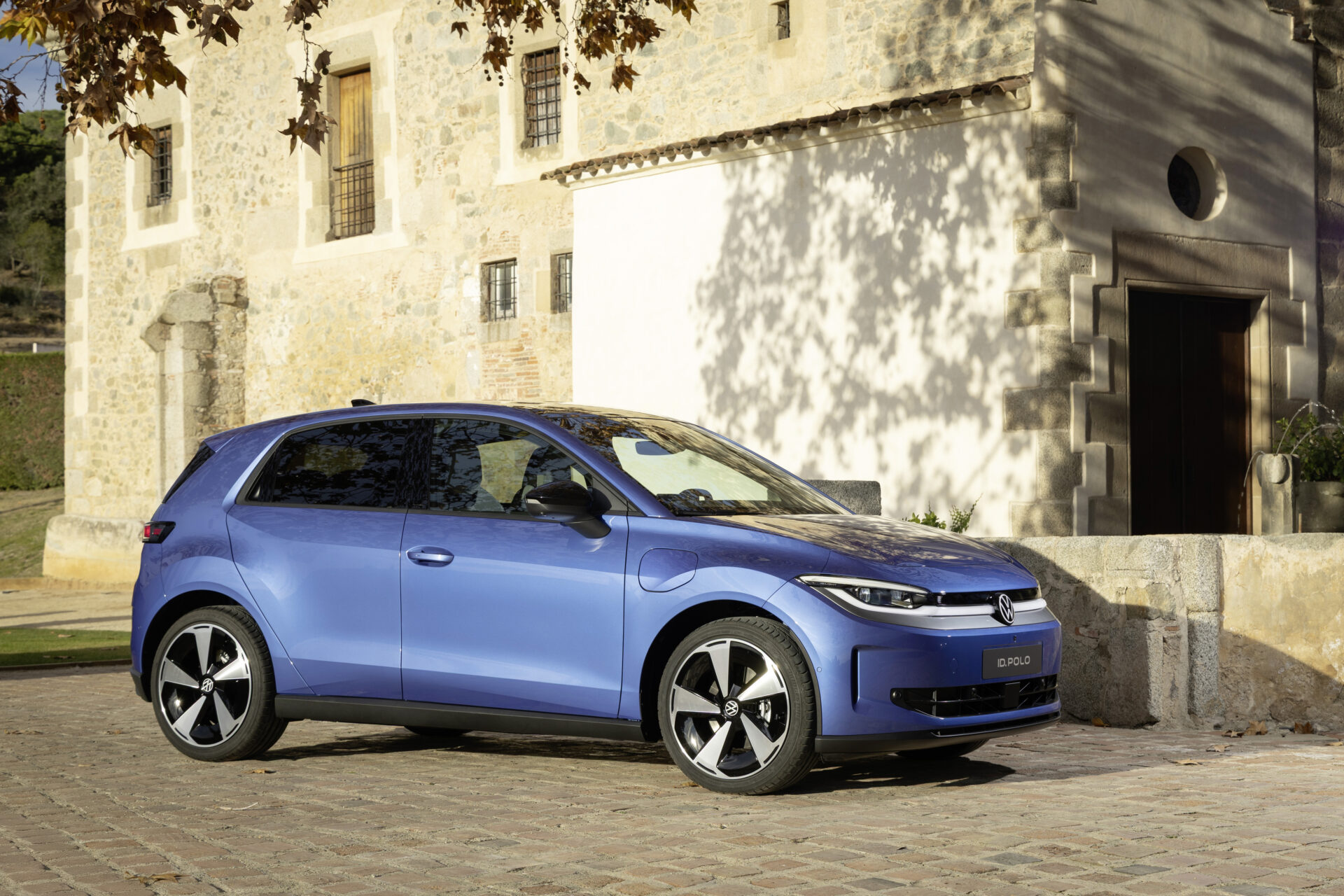 Carro azul modelo Volkswagen ID. Polo estacionado em frente a uma casa de pedra antiga.