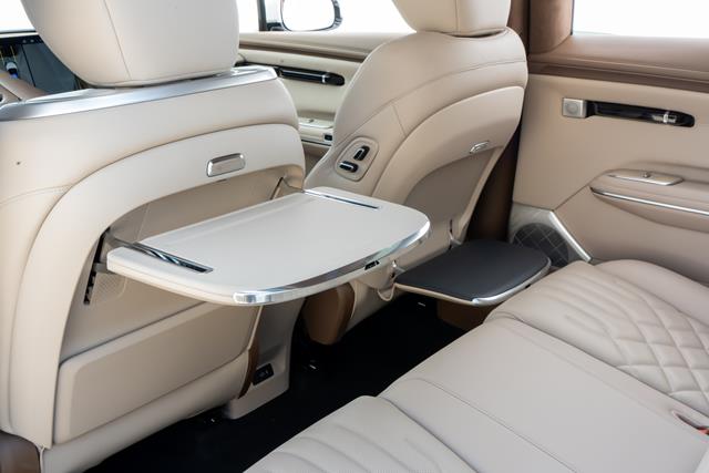 Interior de um carro com bancos de couro bege, destacando uma mesa retrátil instalada no encosto do banco dianteiro.