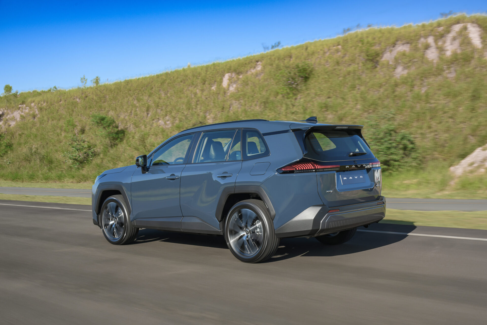 Um SUV moderno em movimento em uma estrada cercada por vegetação, com uma colina ao fundo.