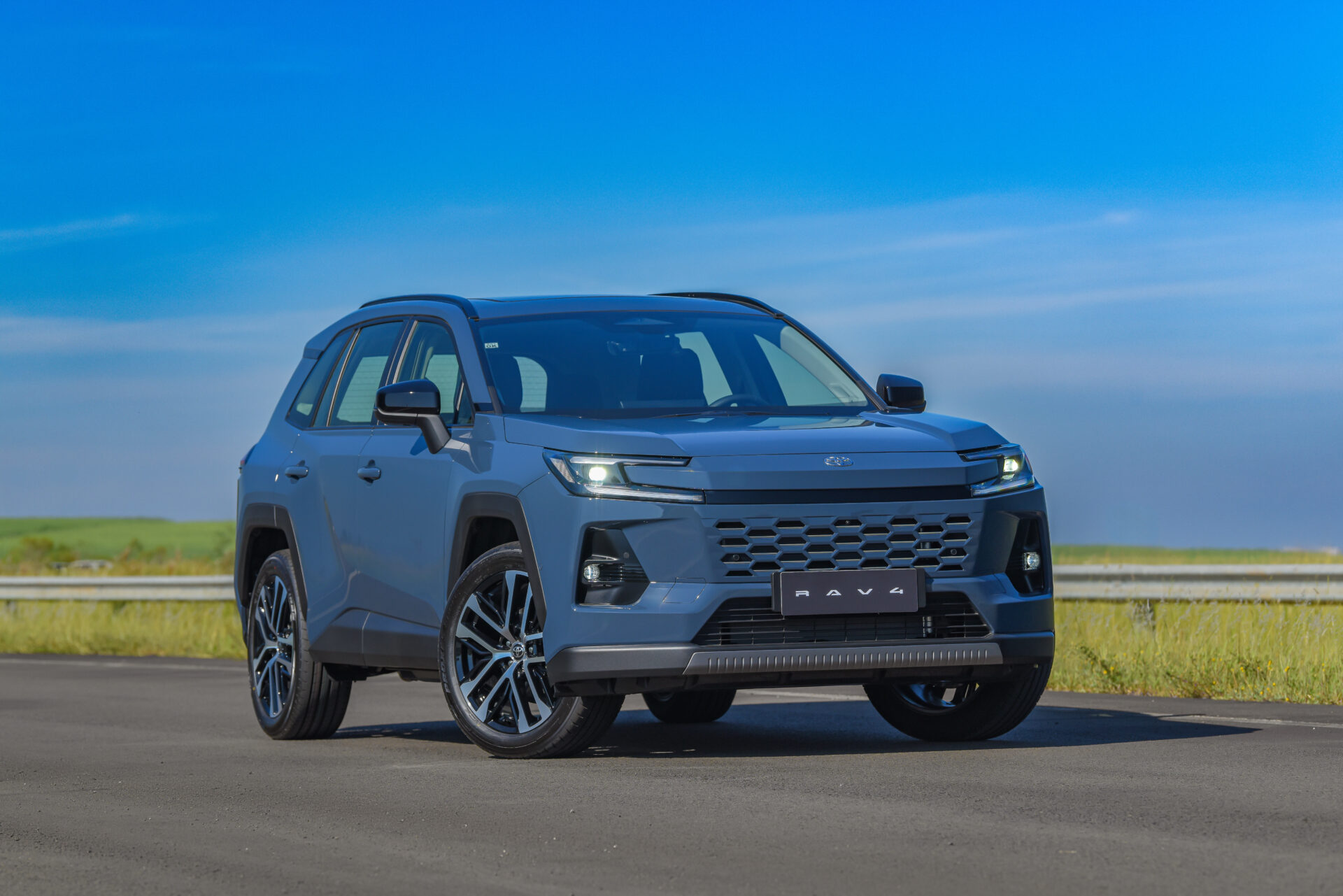 Um carro SUV da Toyota, modelo RAV4, estacionado em uma estrada com céu azul ao fundo.