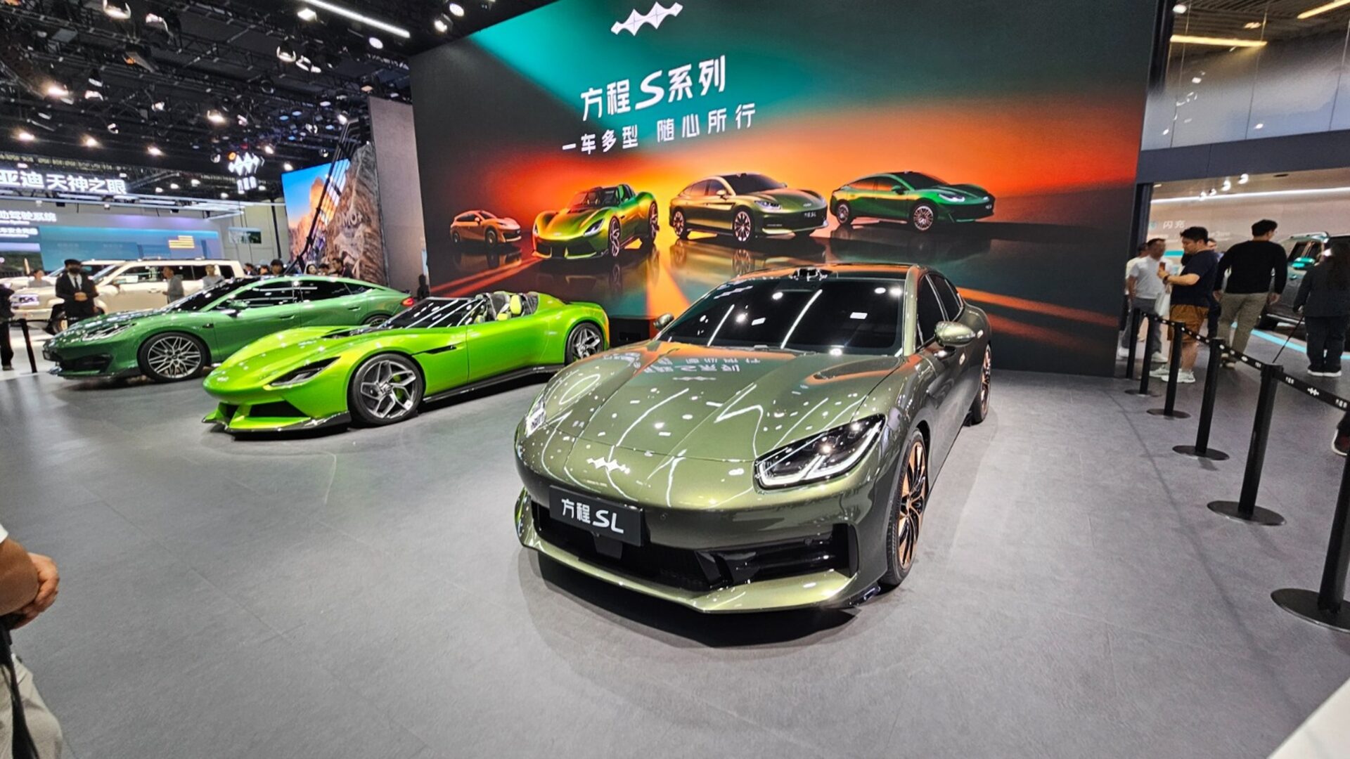 A showcase of three luxury cars at an auto show, featuring a green sports car, a sleek green coupe, and a silver sedan labeled 'SL'. The backdrop displays various car models and designs.