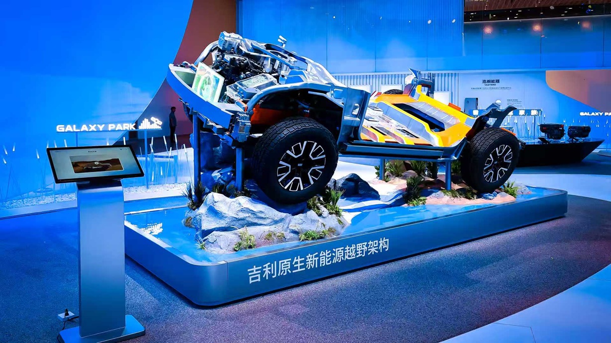 A futuristic vehicle display at Galaxy Park, showcasing a partially assembled car with visible mechanical components, placed on a rocky base with greenery, under blue ambient lighting.