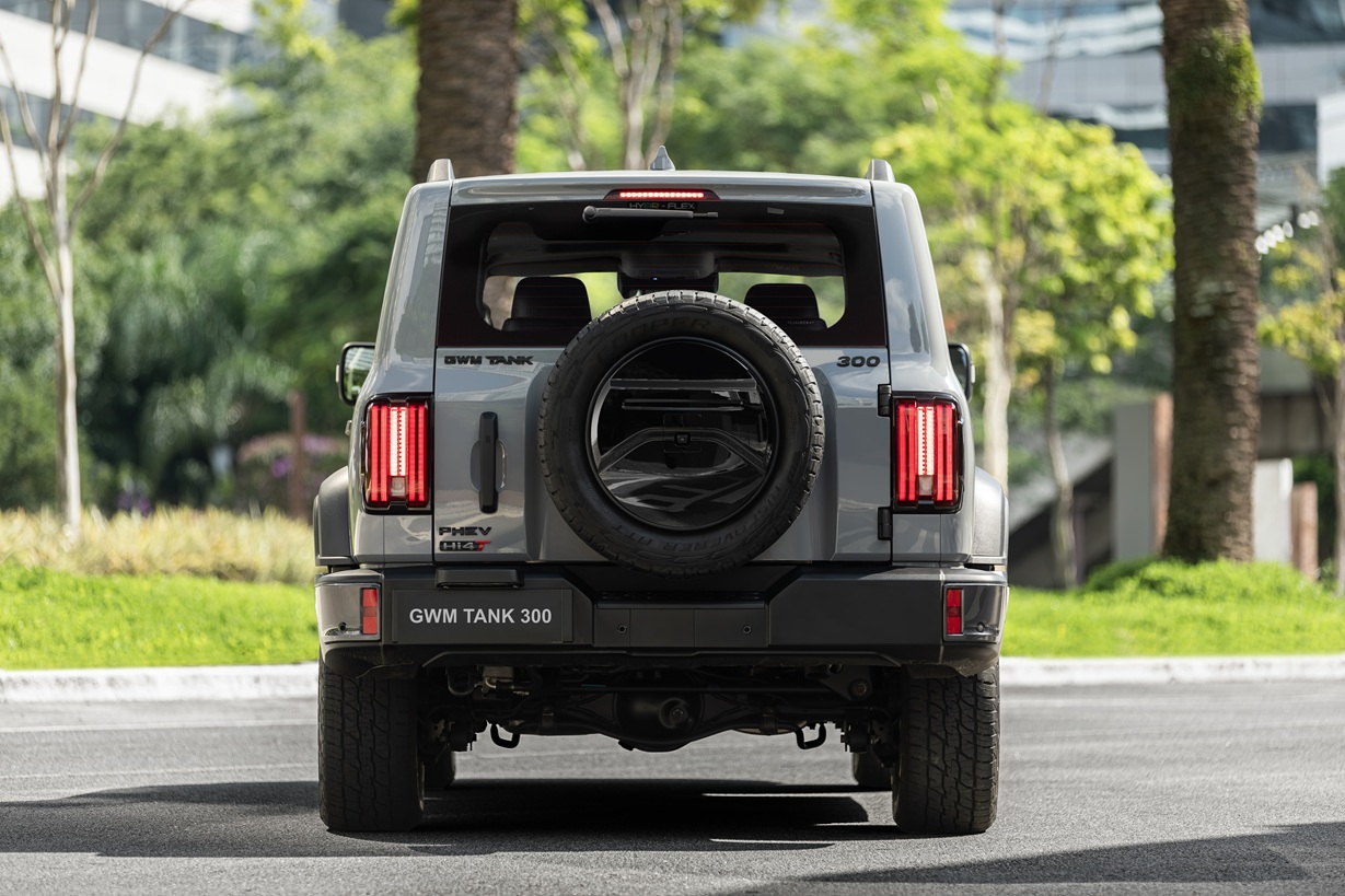 Rear view of a GWM Tank 300 SUV parked on a sunny road, showcasing its spare tire and tail lights.