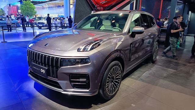 Um SUV de luxo exposto em um salão do automóvel, da marca Lynk & Co, modelo 09, com pintura prata e detalhes elegantes.