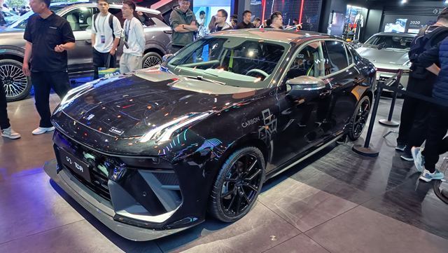 Carro esportivo preto exposto em um evento, com detalhes em verde, rodeado por pessoas observando.