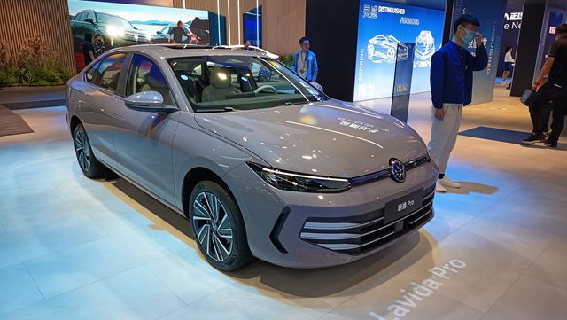 Carro Volkswagen Lavida Pro em exibição, visto de lado, em um ambiente de feira automotiva com fundo iluminado.
