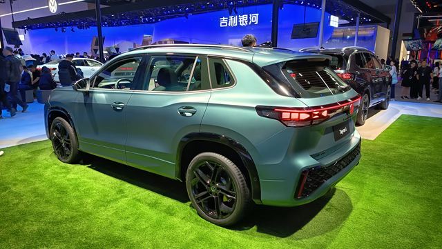 SUV moderno em exibição, pintado em tom verde, com rodas pretas e detalhes acentuados. O veículo está posicionado sobre grama artificial em um ambiente de feira automotiva.