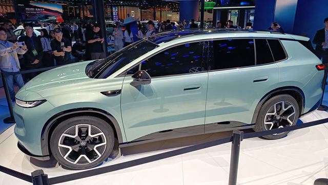 Um SUV de cor verde claro exposto em um salão do automóvel, cercado por espectadores.