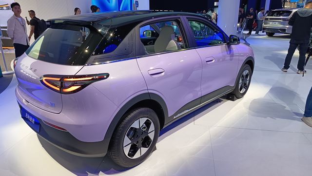 Um carro elétrico de cor lilás exposto em um evento, com destaque para seu design moderno e perfil traseiro.