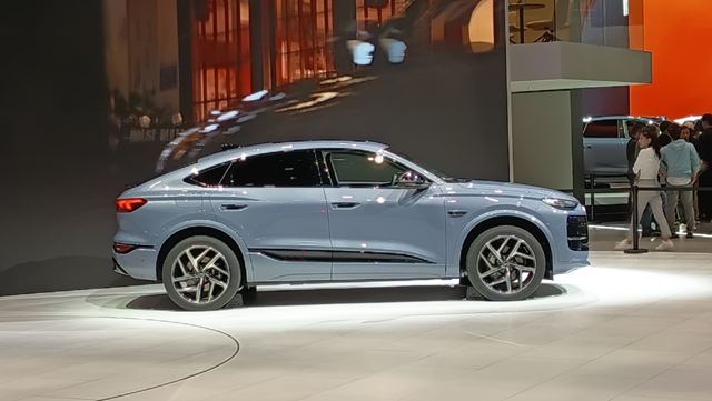 Um carro SUV azul claro em exibição em um evento automotivo, visto de perfil, com fundo neutro.