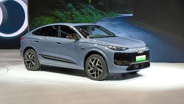 Carro Audi de cor azul claro exibido em um estande de evento automotivo, com fundo de rodovia.