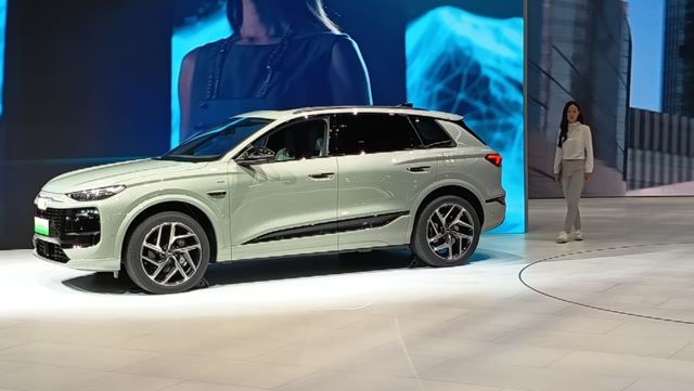 Um SUV branco destacado em um evento de lançamento, com uma mulher ao fundo caminhando em direção ao veículo.