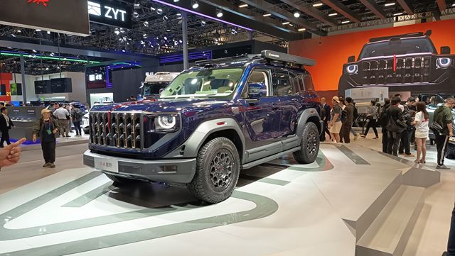 Veículo utilitário esportivo azul exposto em uma feira de automóveis, com destaque para a grade frontal distinta e pneus grandes.