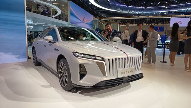 Sedã branco moderno em exibição em um salão automotivo, com design elegante e detalhes sofisticados.