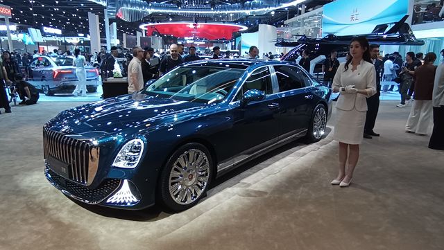 Carro luxuoso em exibição em salão automotivo, com uma mulher apresentando ao lado.
